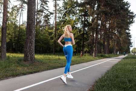 Young athletic woman with sexy ass is jogging in park in summer sunshine. Beautiful woman runner training on nature. Concept of sport, healthy lifestyle, movement, activity. back view.の写真素材