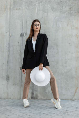 Vogue modern young girl in glasses in casual shoes in stylish clothes and with beautiful white hat...