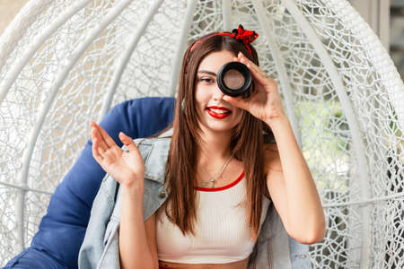 funny woman with a smile holds the lens near the face and sits on the chair eggの写真素材