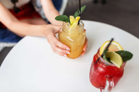 Female hands hold sweet fresh summer fruit lemonade. Two berry drinks with ice and mint slices on...