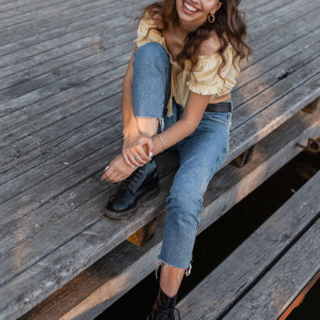 Pretty positive attractive girl with a cute smile in stylish clothes with fashion blue classic jeans, top blouse and leather shoes is resting on the pier on the beach.の写真素材