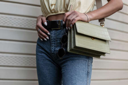 Fashionable woman with trendy blue jeans and leather bag walks on the street. Close-up of female stylish handbag and classic jeans with sunglassesの写真素材