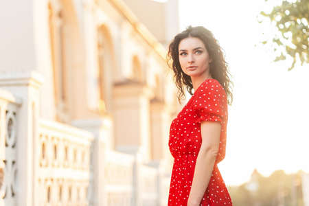 summer portrait of a beautiful young woman in a fashion red dress in the city at sunset