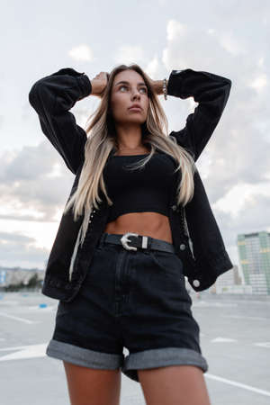 Fashion beautiful woman model in a black stylish denim jacket with rhinestones in denim shorts and a black top posing in the cityの写真素材