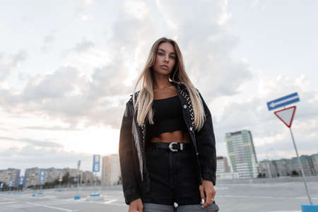 Young beautiful girl model with a cute face in a black denim jacket with black jeans and a top undershirt walks in the cityの写真素材