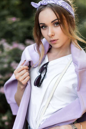 Portrait of beautiful hipster woman with sunglasses in white t-shirt with purple sweatshirt on nature near flowersの写真素材