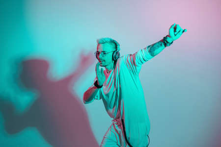 Hipster man listen to music and dances on a colorful pink and blue background. Fashion guy with headphones moving in the rhythm of dance in studioの写真素材