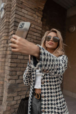 Glamorous beautiful young girl in fashionable clothes with glasses and a handbag makes a selfie...