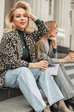 Stylish beautiful young girls hipster girlfriends in fashionable clothes sitting on the steps outside a vintage buildingの写真素材