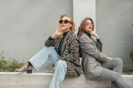 Beautiful young fashionable women friends in trendy autumn clothes with sunglasses, leopard jacket,...