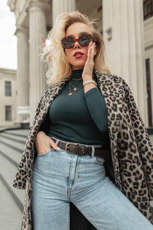Stylish beautiful glamorous blonde hipster girl puts on fashion sunglasses in the cityの写真素材