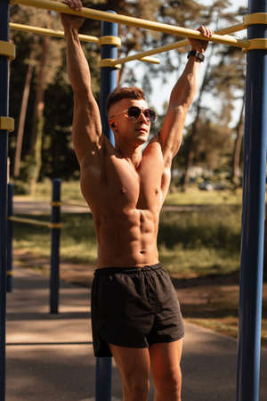 Strong sports man model with sunglasses and wireless headphones exercise and workout in the park....
