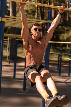 Beautiful young sports man with a muscular body does exercises on the horizontal bar in the park....