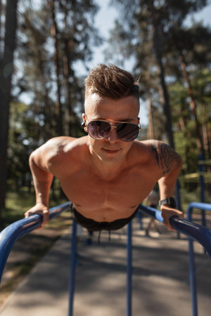 Cool strong sporty man with muscular body and push-ups on horizontal bars outdoors
