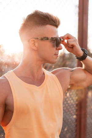 Stylish male portrait of handsome young hipster guy with hairstyle and muscular body wearing fashion sunglasses and looking to the side at sunsetの写真素材