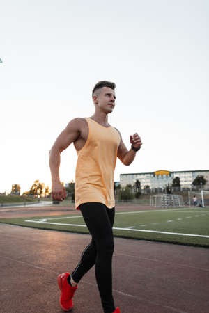 Handsome young athlete man in sportswear with red shoes running on treadmill in stadiumの写真素材