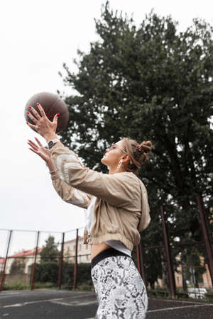 Beautiful fashionable young woman model in fashion clothes plays and tosses the ball on the...