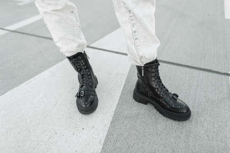 young stylish woman in fashionable black leather boots shoes with light-colored jeans is standing on...