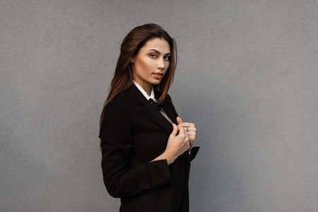 Fashionable beautiful girl in a fashionable black business suit with a jacket on a gray background...