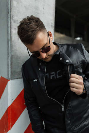 Stylish street man model with hair with black sunglasses wearing black clothes with a black leather...