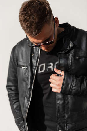Trendy young handsome man hipster with hairstyle in black clothes with leather jacket, t-shirt and...