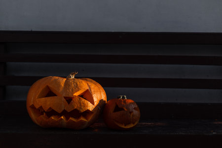Scary Halloween pumpkins standing on a garden bench near a wall at eveningの写真素材