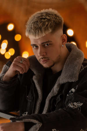 Fashionable serious man hipster with hairstyle in black fashion clothes with jacket indoors in the mallの写真素材