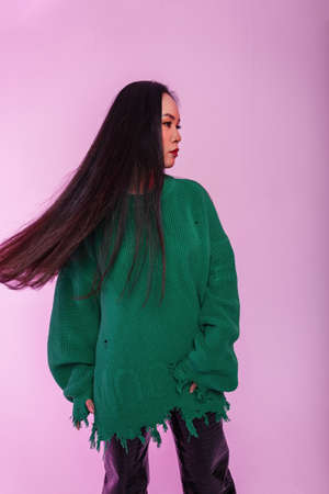 Beautiful young stylish woman model with healthy hair in a fashionable green knit sweater with leather pants on a green background in the studioの写真素材