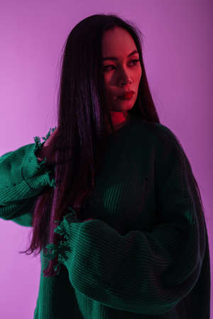 Fashionable young woman model with green stylish knitted sweater with pink light in studioの写真素材