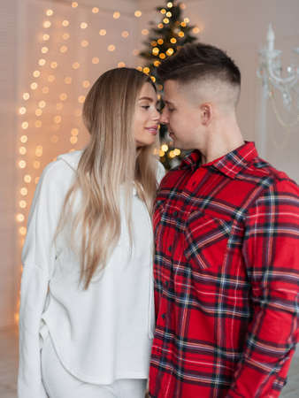 Young beautiful couple in love in fashion home clothes preparing for a kiss at home against a backdrop of Christmas lightsの写真素材
