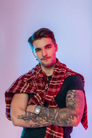 Cool handsome hipster man with tattoos on arms and hairstyle in fashion vintage clothes with plaid...