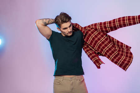 Cool fashionable handsome American hipster man in stylish clothes wears a plaid shirt in a studio with colorful creative lightingの写真素材