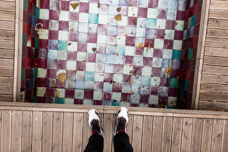 Man stands on a wooden bridge near a fountain with a pool of colored vintage tiles in Lisbon, Portugal. Man's feet with sneakers by the pool, top viewの写真素材