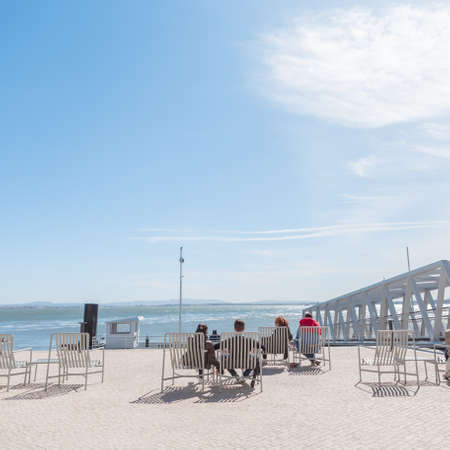 Tourists people sit in chairs near the pier promenade by the sea and enjoy the sunny weather....
