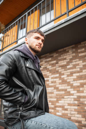 Fashionable handsome young guy hipster model with hair and beard in stylish clothes with hoodie and...