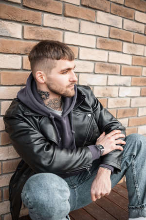 Stylish handsome American model hipster guy with hair and tattoos on his neck in fashionable casual...