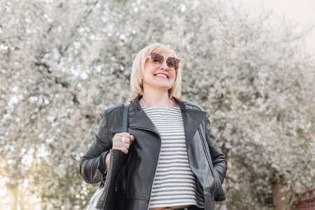Beautiful elderly happy fashionable woman with sunglasses in fashion clothes and a leather jacket...