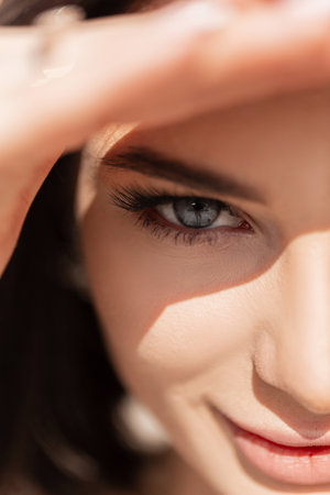 Stylish beautiful young girl with amazing blue eyes covers her face from the sunlight and looks at the camera on a summer sunny day. half female fresh faceの写真素材