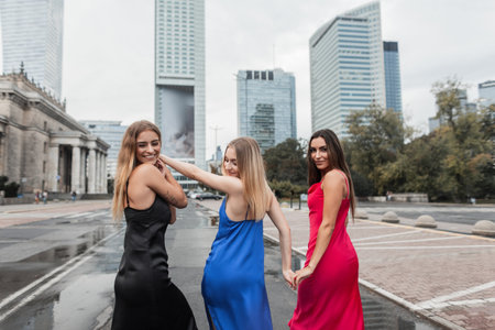 Tee happy beautiful fashionable girls in stylish elegant dresses are walking and having fun in the city, back viewの写真素材