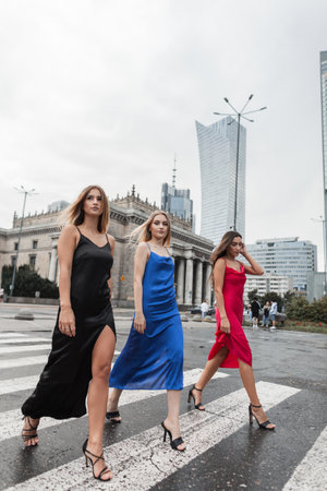 Fashionable beautiful stylish woman girlfriends in elegant fashion dresses are walking on crosswalk in the cityの写真素材