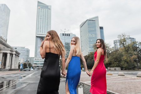Three beautifully elegant urban happy girls in fashion stylish dresses walk together holding hands in the cityの写真素材