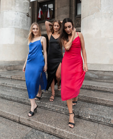 Beautiful fashion three girl friends in a fashionable strappy dress with heels are walking down the steps in the city.の写真素材