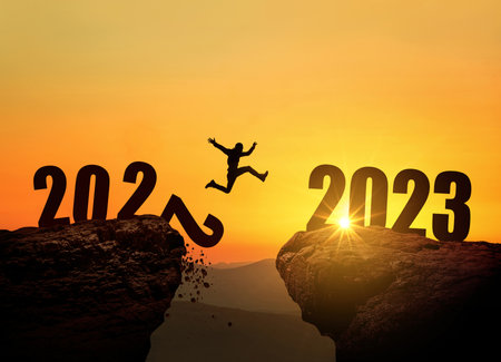 Man jumping on cliff 2023 over the precipice with stones at amazing sunset. New Year's concept. 2022 falls into the abyss. Welcome 2023. People enters the year 2023, creative idea.の写真素材