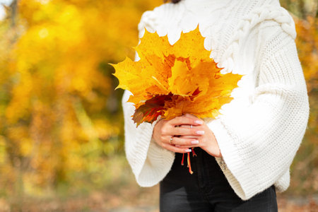 beautiful young girl in a fashionable white knitted sweater holds a fall bouquet of brightly colored...