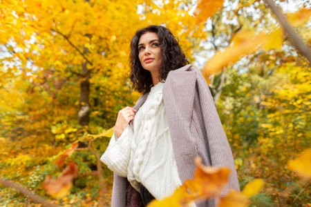 Beautiful curly autumn girl model in a fashionable coat with a knitted sweater walking in the autumn...