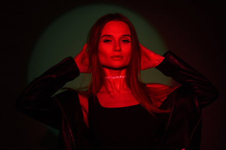 Cool fashionable trendy creative portrait of beautiful woman with red light on a dark green backgroundの写真素材