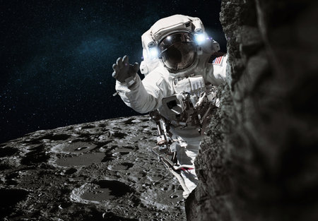 Space man in a suit travels on the moon and climbs uphill. Cosmic mission and moon exploration. Astronaut explores on an asteroid and waves helloの写真素材