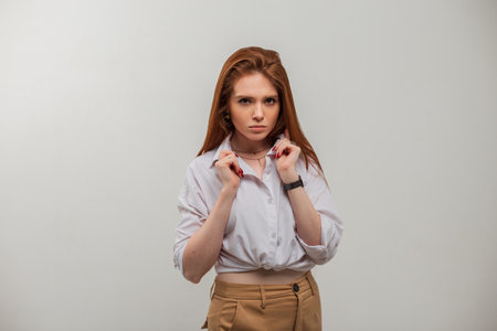 Fashion beautiful redhead girl model in a stylish white shirt on a white background in the studio