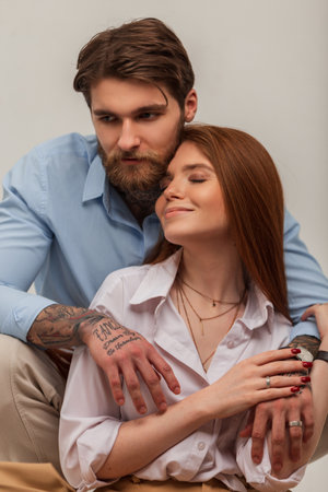 Happy beautiful tender young couple in the studio. Beautiful happy tender red-haired girl and brutal hipster handsome manの写真素材