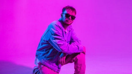 Stylish handsome hip hop dancer guy with sunglasses in trendy fashion denim clothes in color studio...
